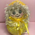 عروسک دست دوز پارچه‌ای دست ساز زرد با موهای سفید پفی و روبان زرد (اگر رنگ یا مدل عوض شد فقط رنگ و ویژگی اصلی رو تغییر بده، مثلاً: عروسک دست‌دوز پارچه‌ای دست‌ساز قرمز با دامن توری)