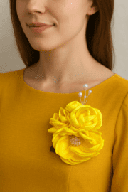 گل‌سینه زرد روباندوزی با مرکز مرواریدی و نگین‌های شفاف روی لباس زنانه رسمی